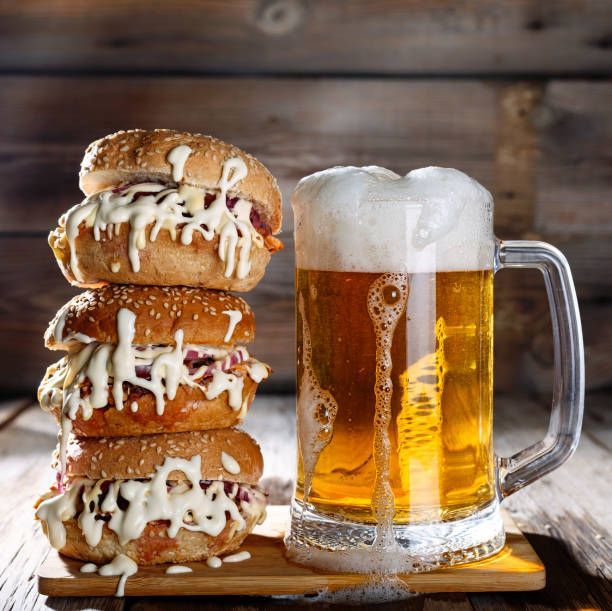 Stack of sandwiches with dripping sauce next to a full mug of beer.
