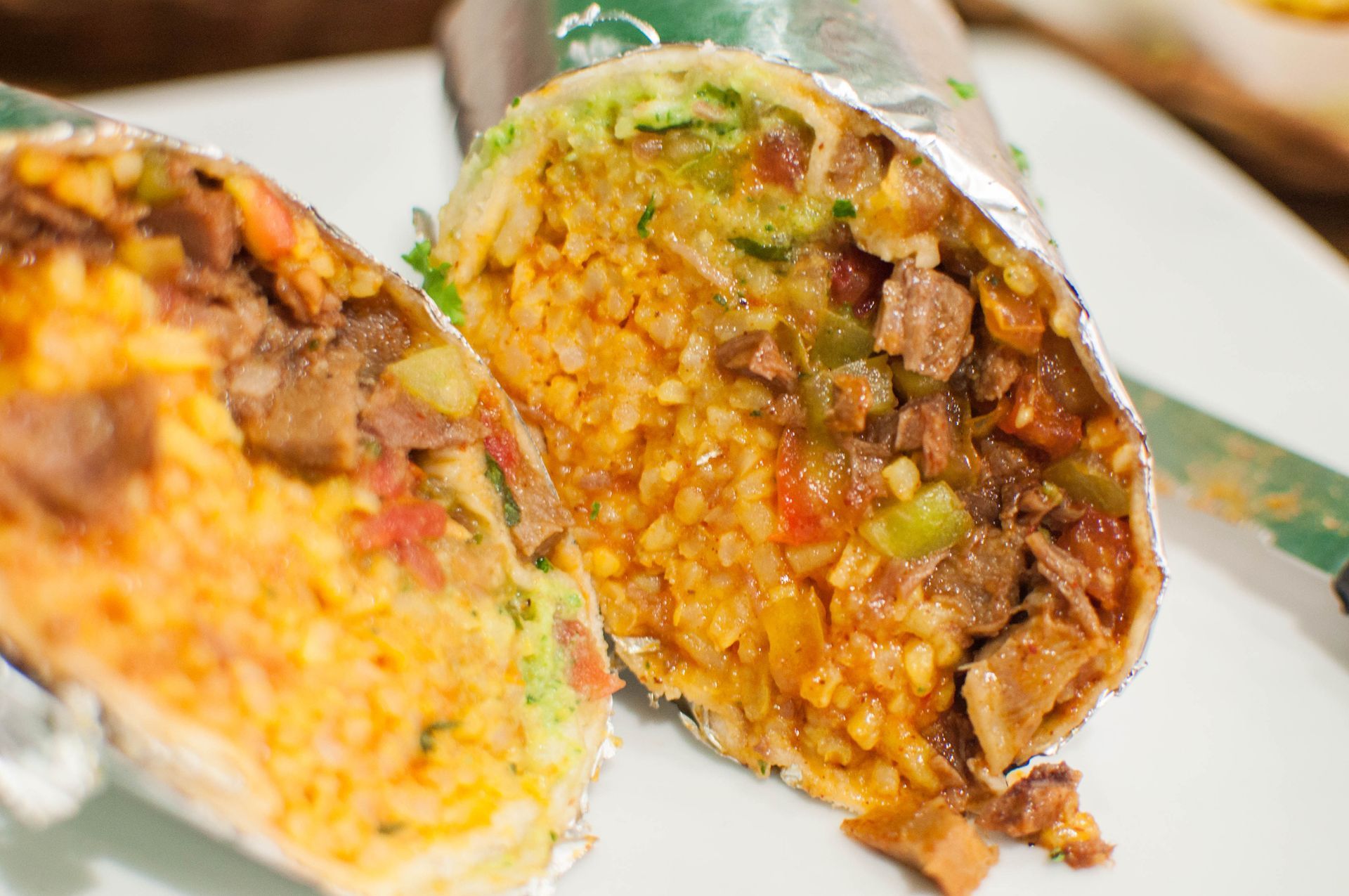 Cut burrito halves, showing rice, meat, guacamole, and salsa fillings wrapped in foil.