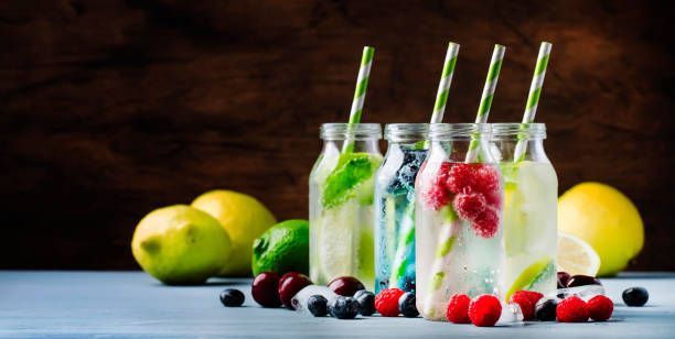 Bottles of fruit-infused water with straws, fruit, and lemons on a wooden surface.