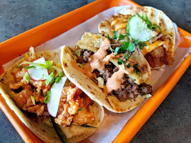 Three tacos on a tray: one with chicken, one with beef, and one with fish, on a orange tray.
