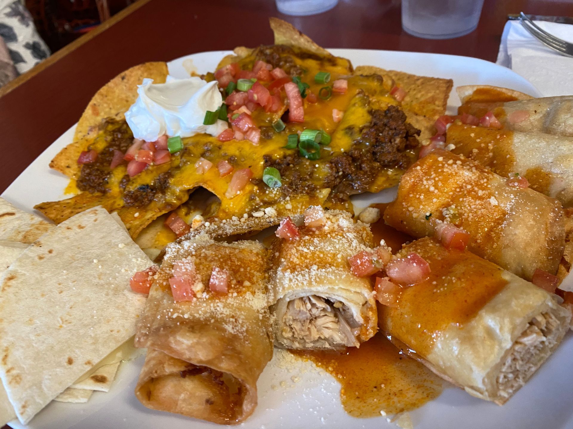 Plate of nachos, taquitos, and tortillas; topped with cheese, meat, and salsa.