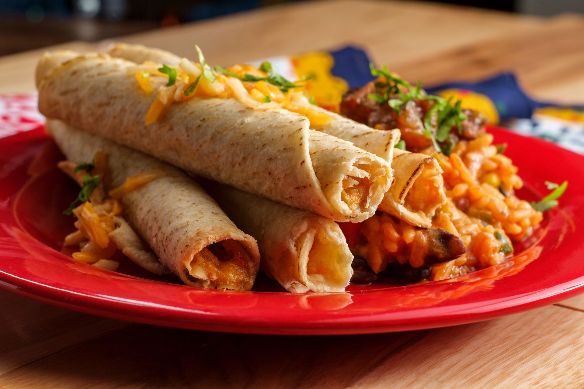 Taquitos topped with cheese, served on a red plate with rice.