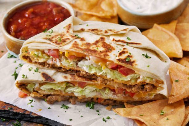 Cut-open burrito with ground meat, lettuce, and tomatoes, served with salsa, sour cream, and tortilla chips.