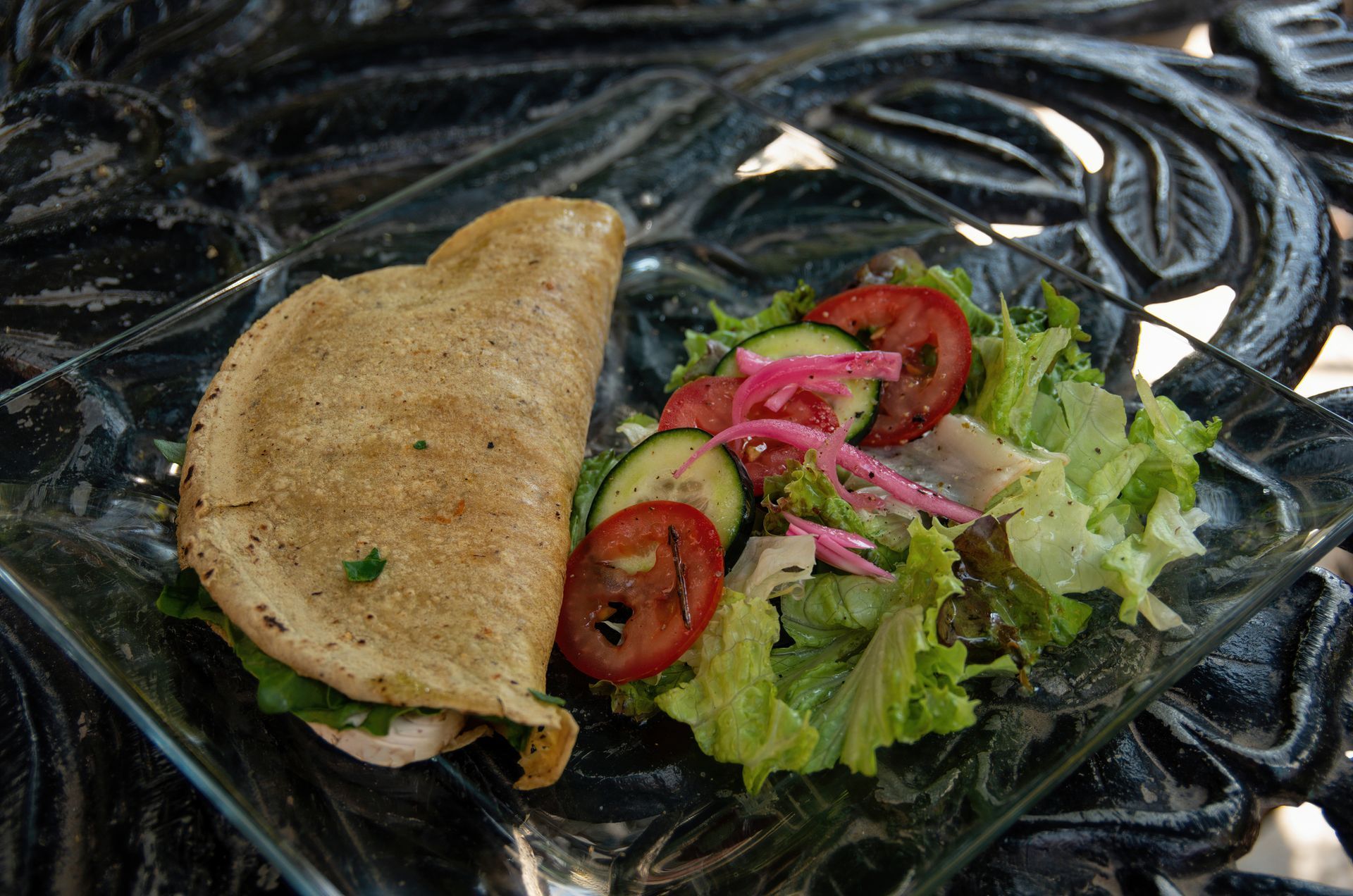 Quesadilla and salad on a glass plate, resting on a dark, patterned surface. Quesadilla and salad on a glass plate, resting on a dark, patterned surface.