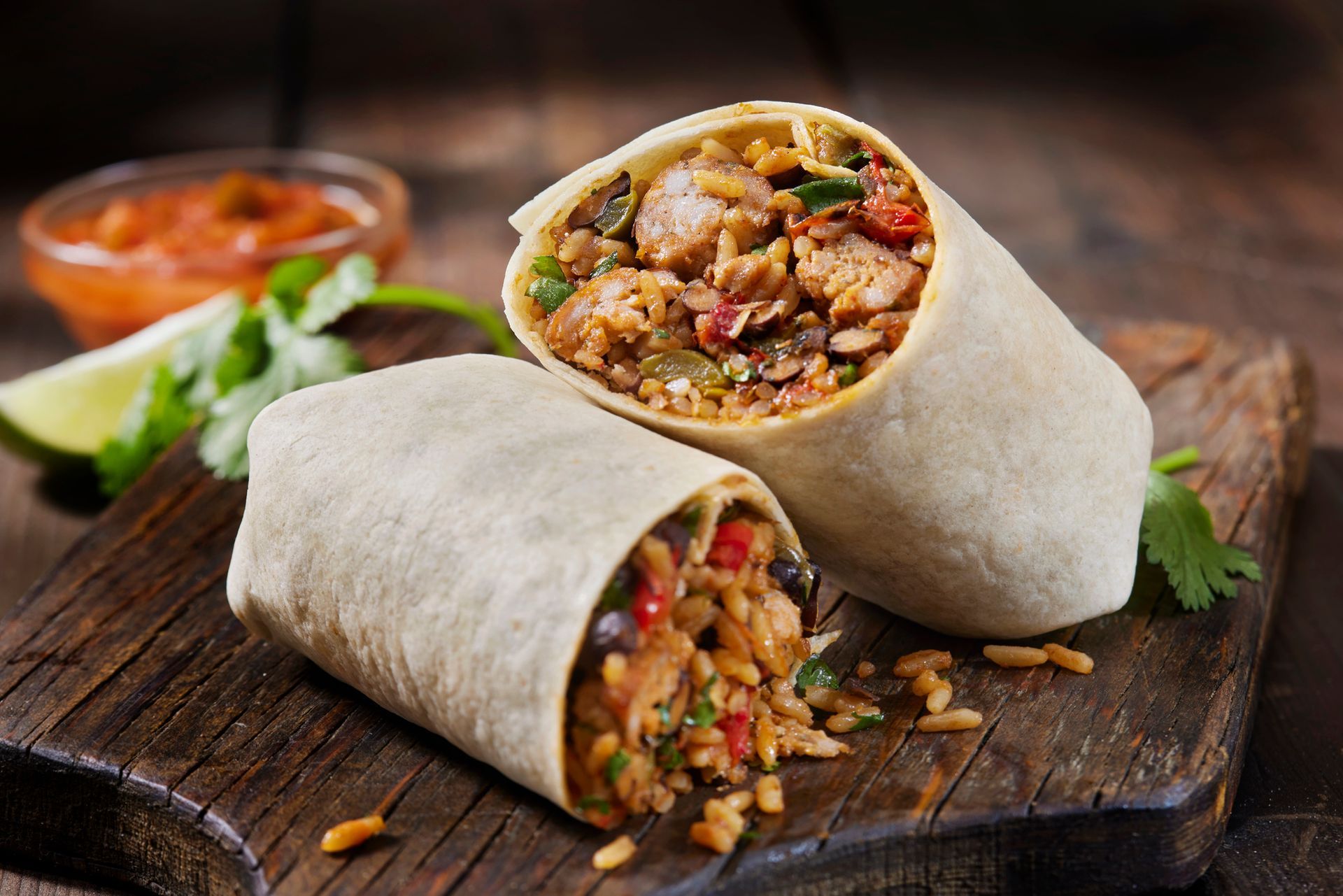 Burrito cut in half, showcasing fillings of rice, vegetables, and meat, on a wooden board.