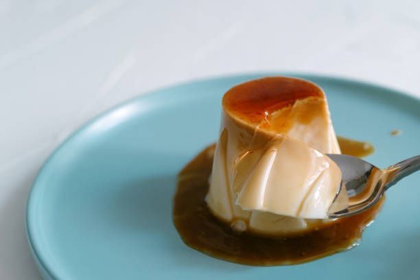 Flan dessert on blue plate with a spoonful being taken out; caramel sauce.