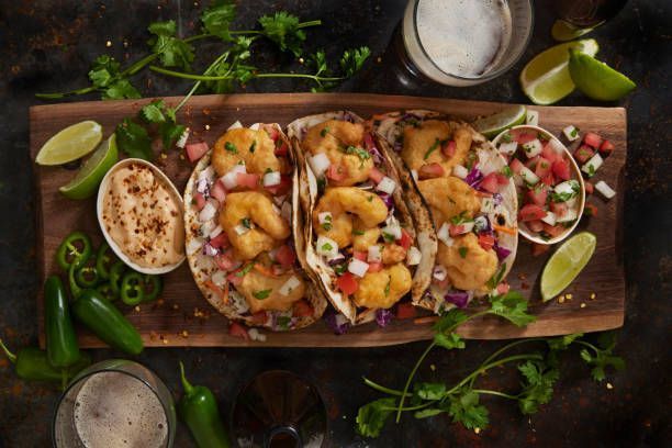 Three shrimp tacos with salsa on a wooden board, garnished with limes and cilantro.