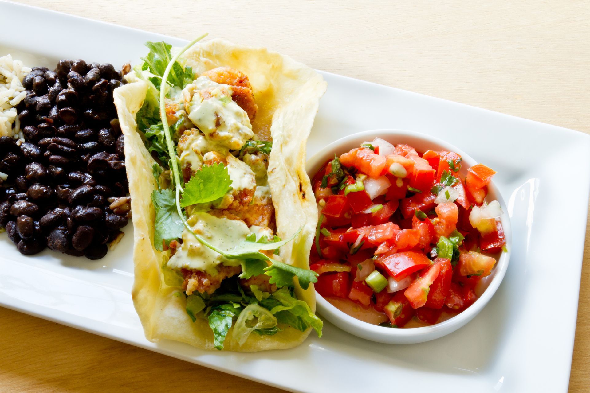 Fish taco with black beans and salsa on a white plate.