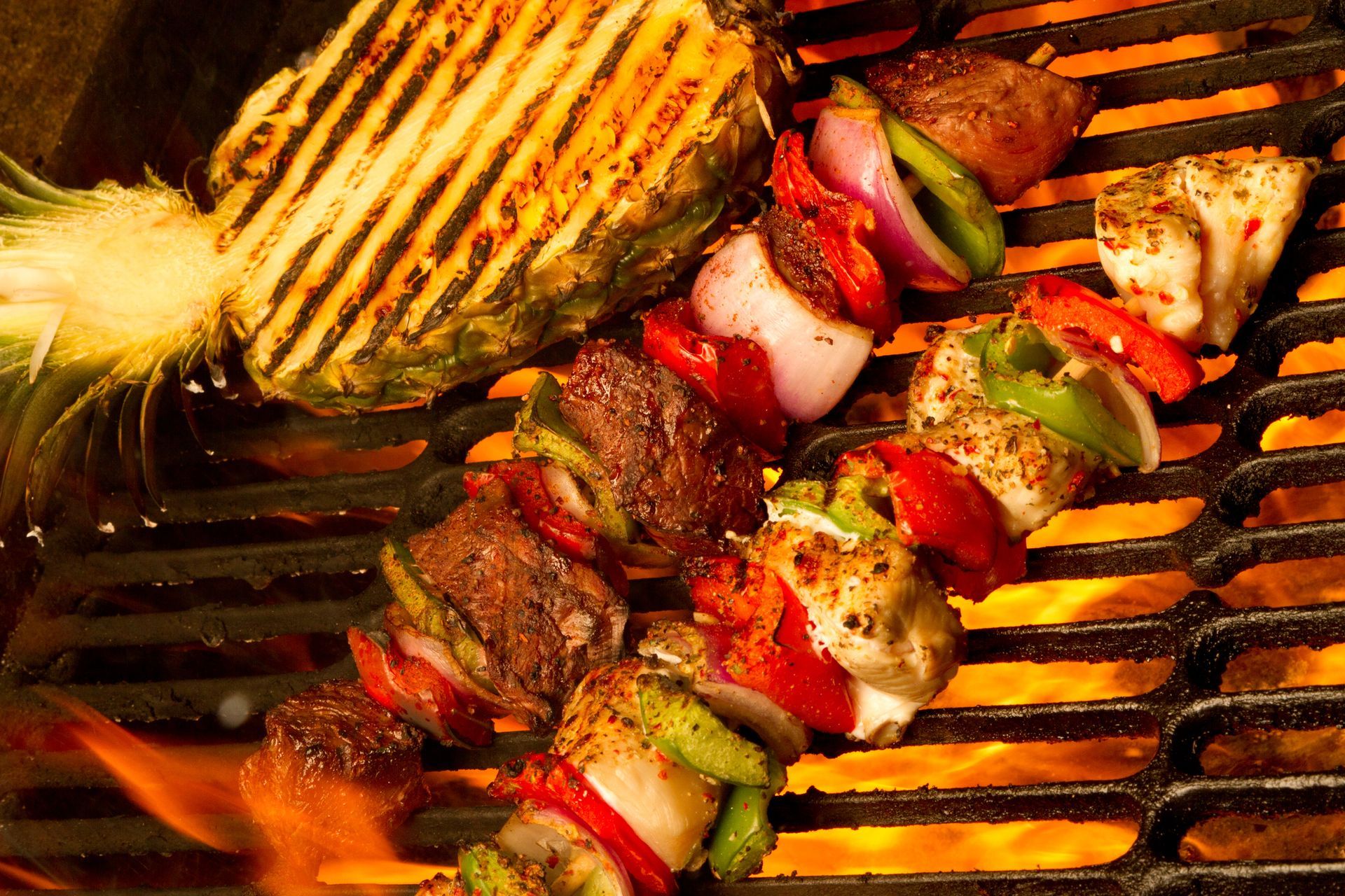 Grilled skewers with beef, vegetables, and pineapple cooking on a hot grill with flames. Grilled skewers with beef, vegetables, and pineapple cooking on a hot grill with flames.