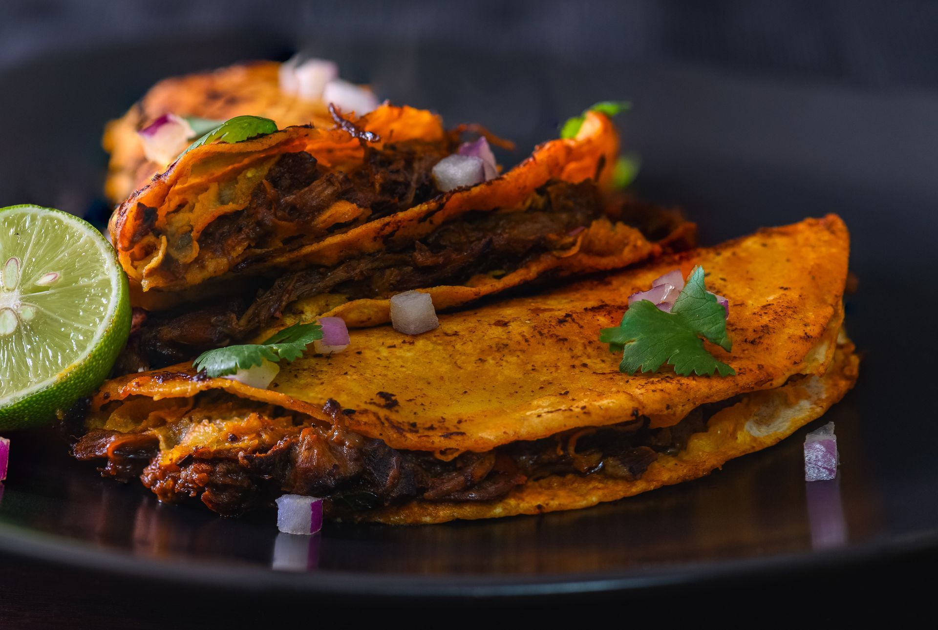 Crispy tacos on black plate with lime, red onions, and cilantro. Crispy tacos on black plate with lime, red onions, and cilantro.