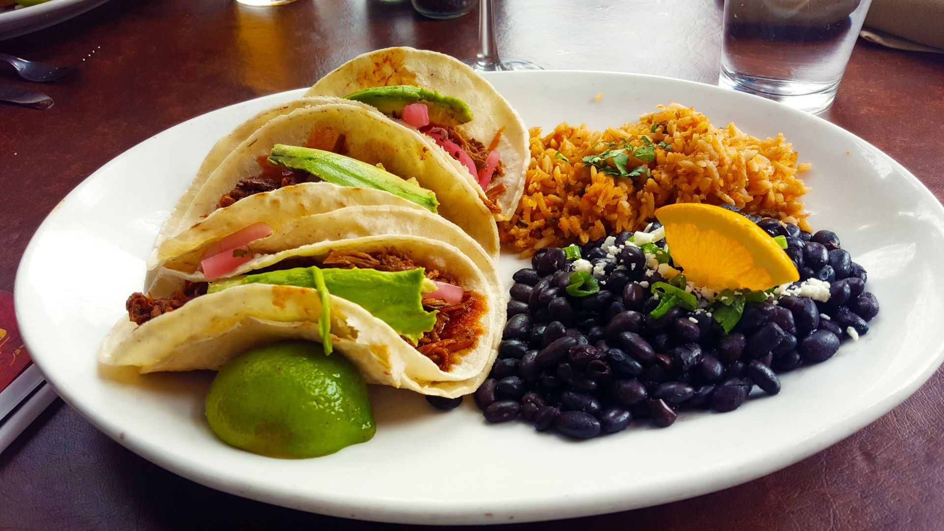 Plate of tacos with rice, black beans, and lime.