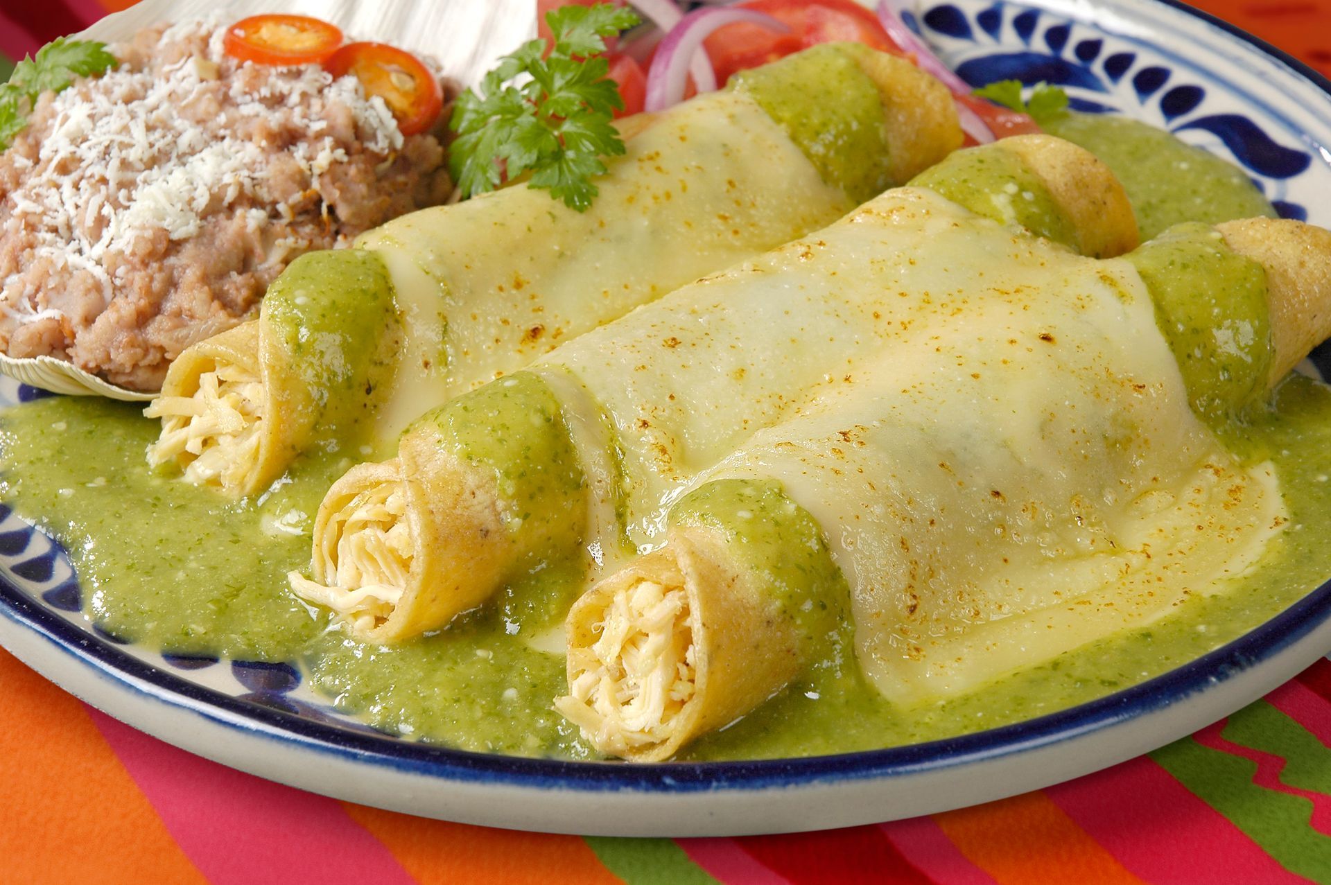 Enchiladas with green sauce, served with refried beans and tomato and onion garnish.