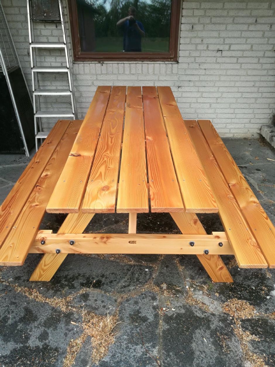 Et picnicbord i træ sidder foran en murstensbygning.