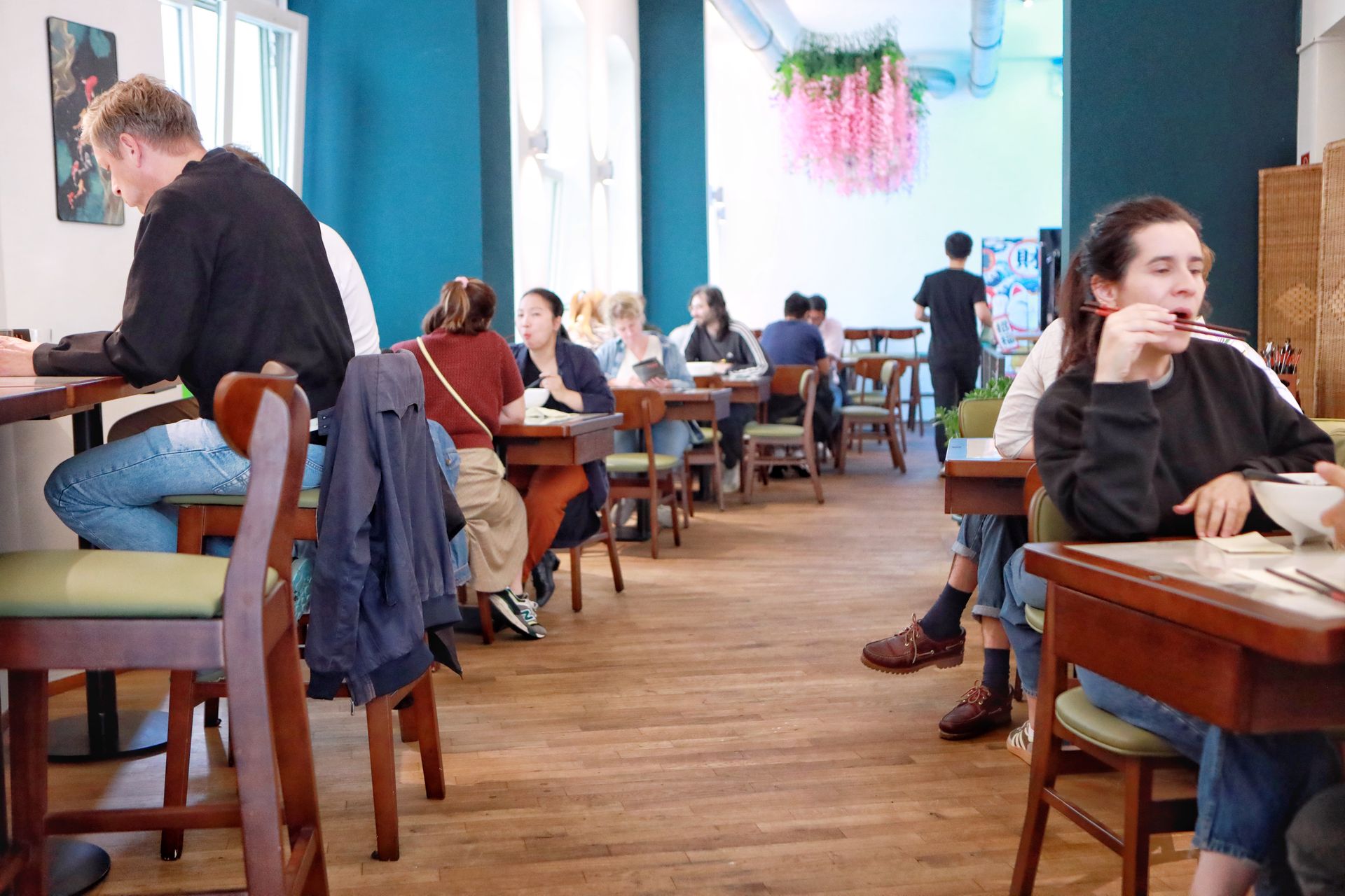 Menschen sitzen und unterhalten sich in einem hellen Café mit Holztischen und -stühlen