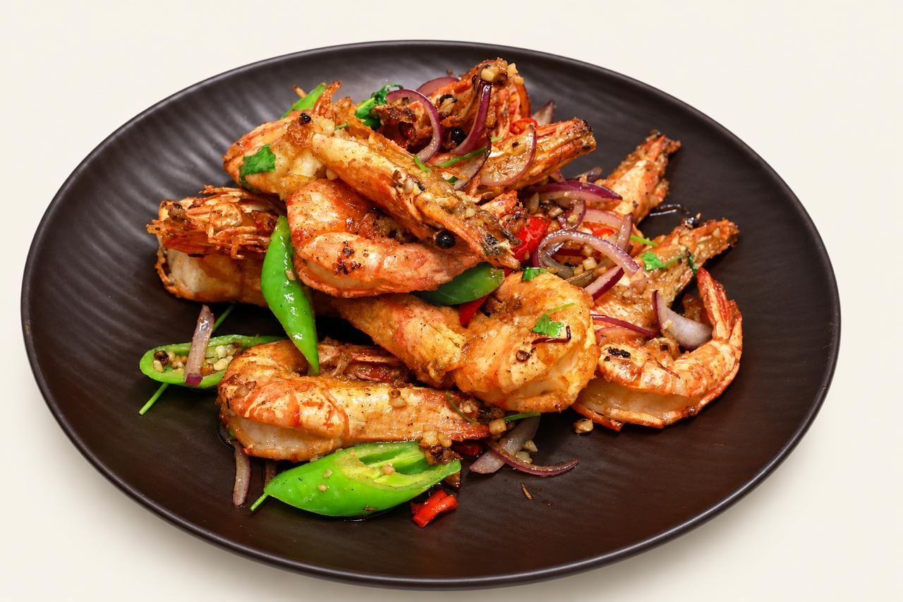 Teller mit gegrillten Garnelen, grüner Paprika und Zwiebeln auf einem dunklen Teller