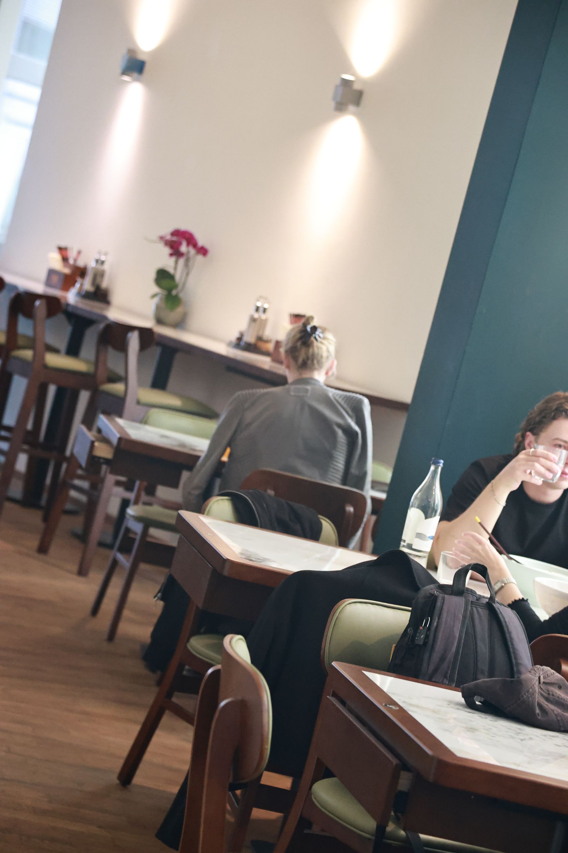 Café-Innenraum mit sitzenden Gästen an kleinen Tischen unter Wandleuchten und einer petrolfarbenen Trennwand