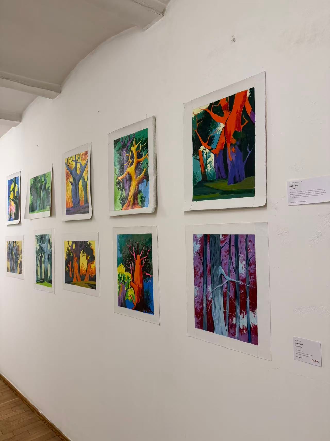 Galeriewand mit farbenfrohen abstrakten Gemälden in weißen Rahmen entlang eines weißen Flurs.