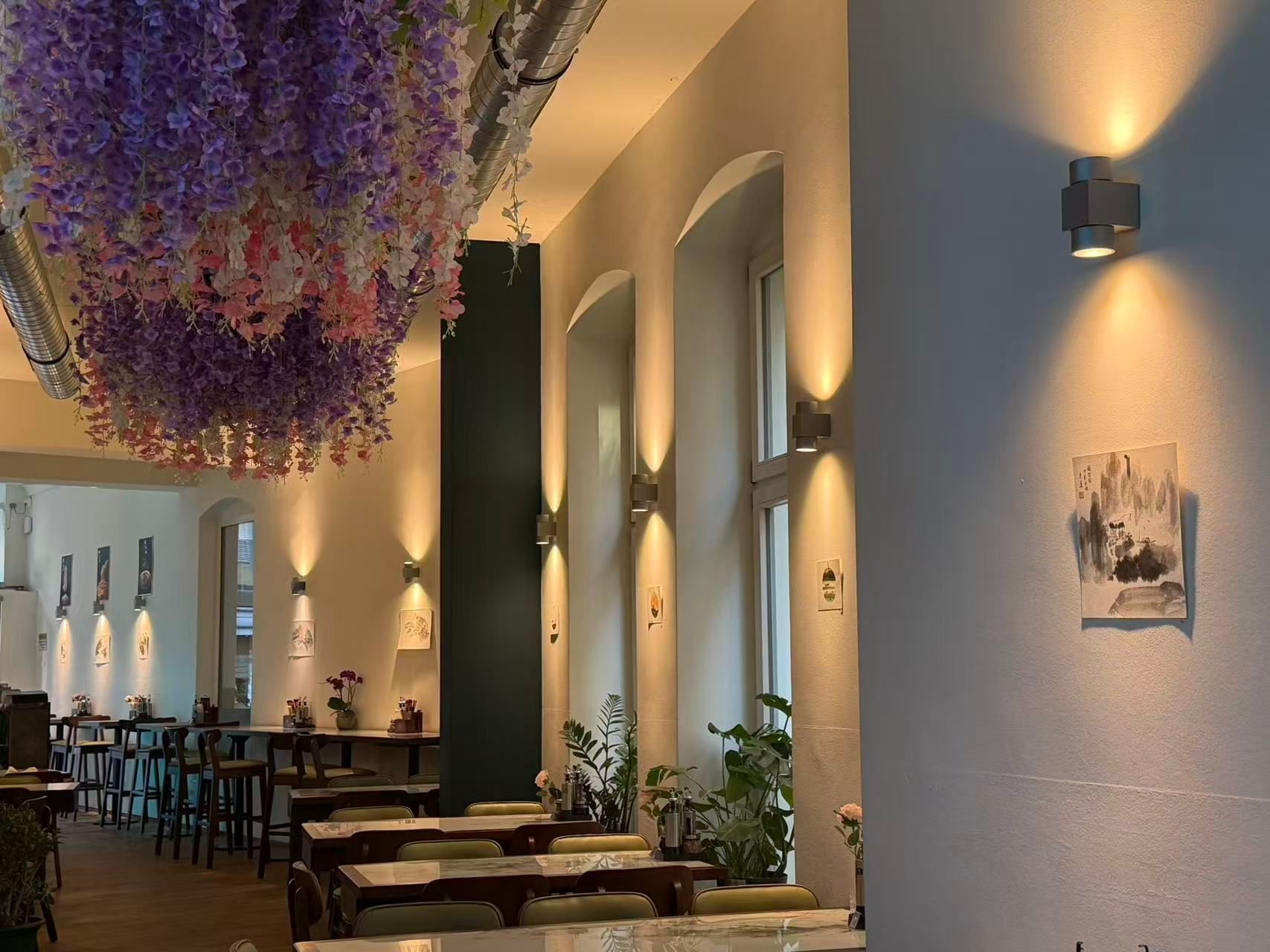 Elegantes Restaurantinterieur mit geschwungenen Wandleuchten, Holztischen und hängenden violetten Blumen