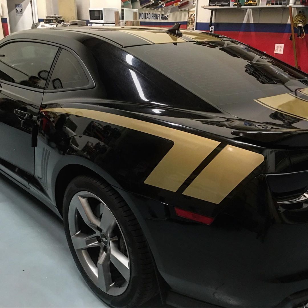 A black car with gold stripes on the side is parked in a garage