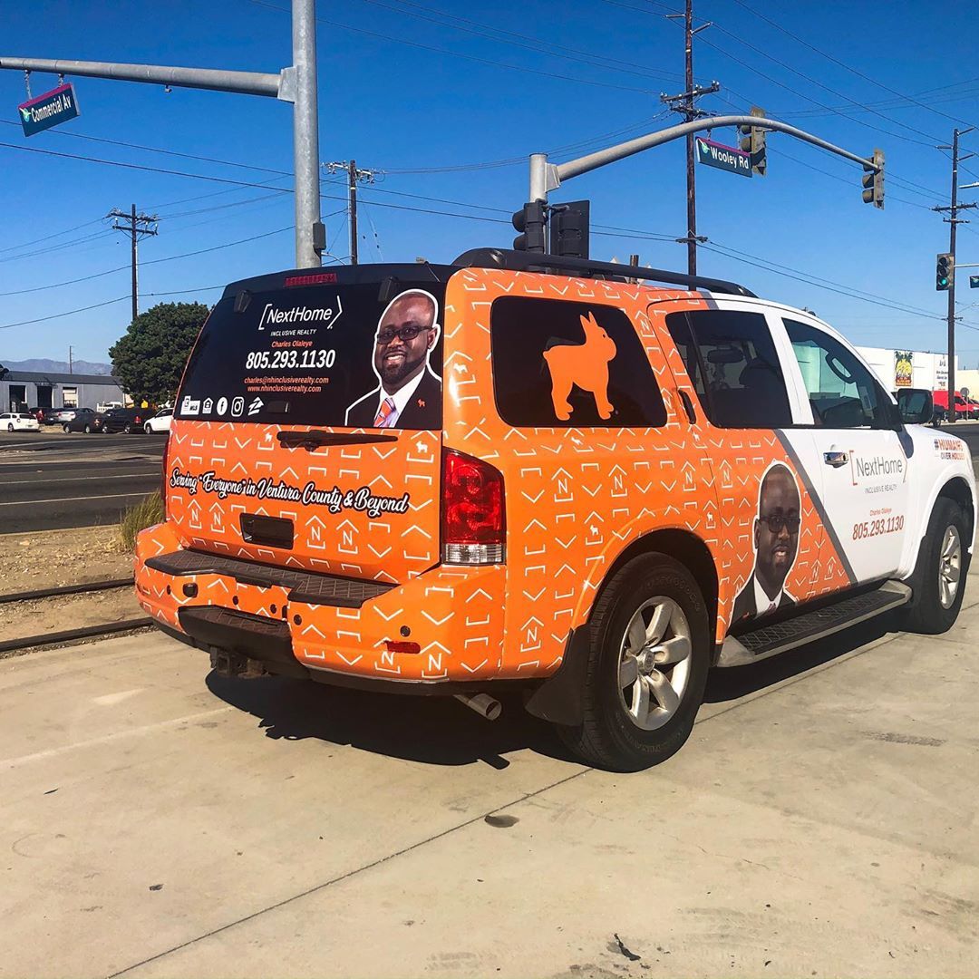 An orange suv with a picture of a man and a dog on the back is parked on the side of the road