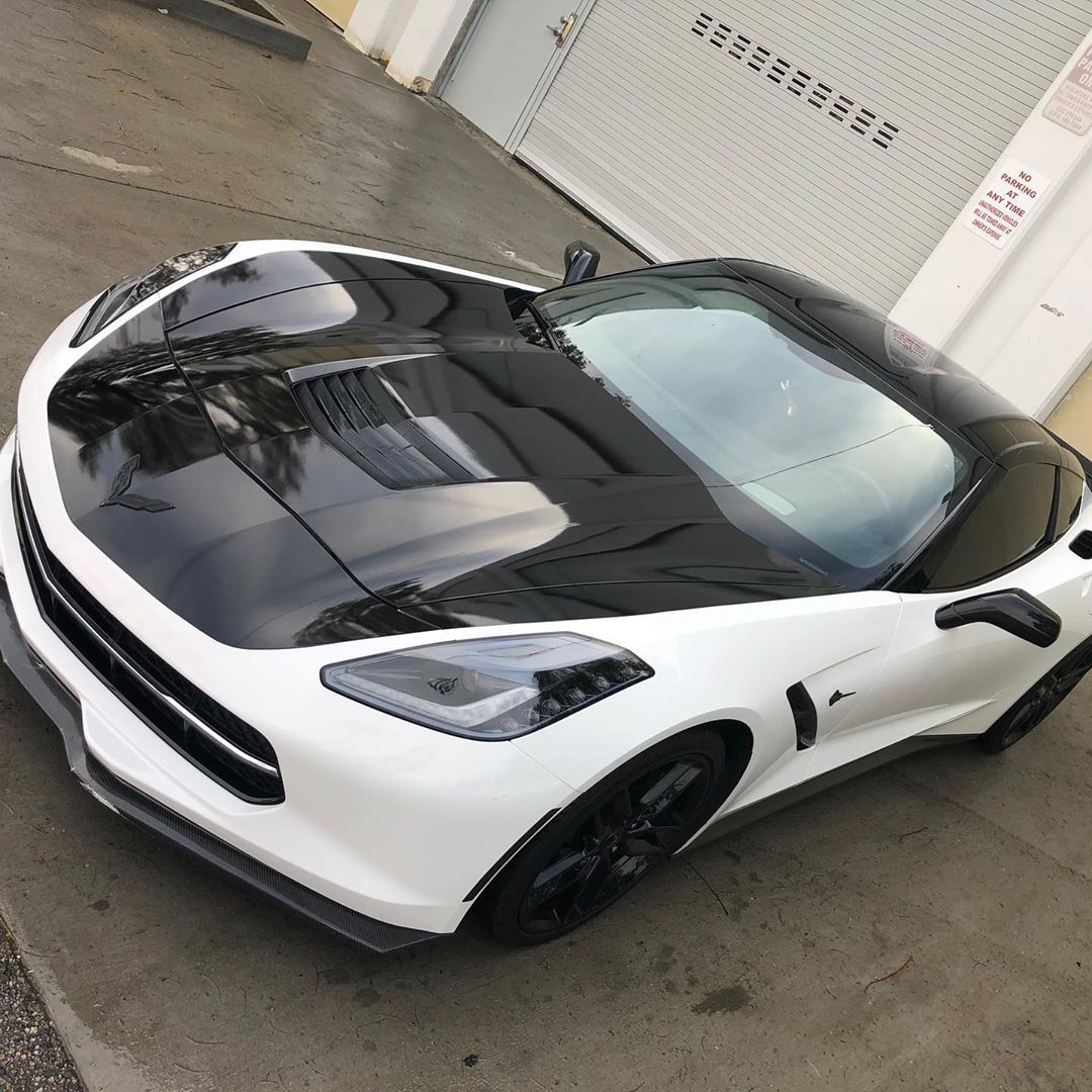 A white sports car with a black hood is parked on the side of the road.