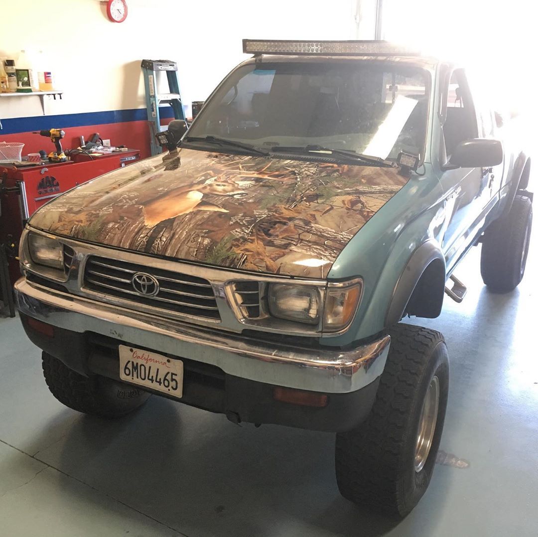A toyota truck with a camouflage hood is parked in a garage.