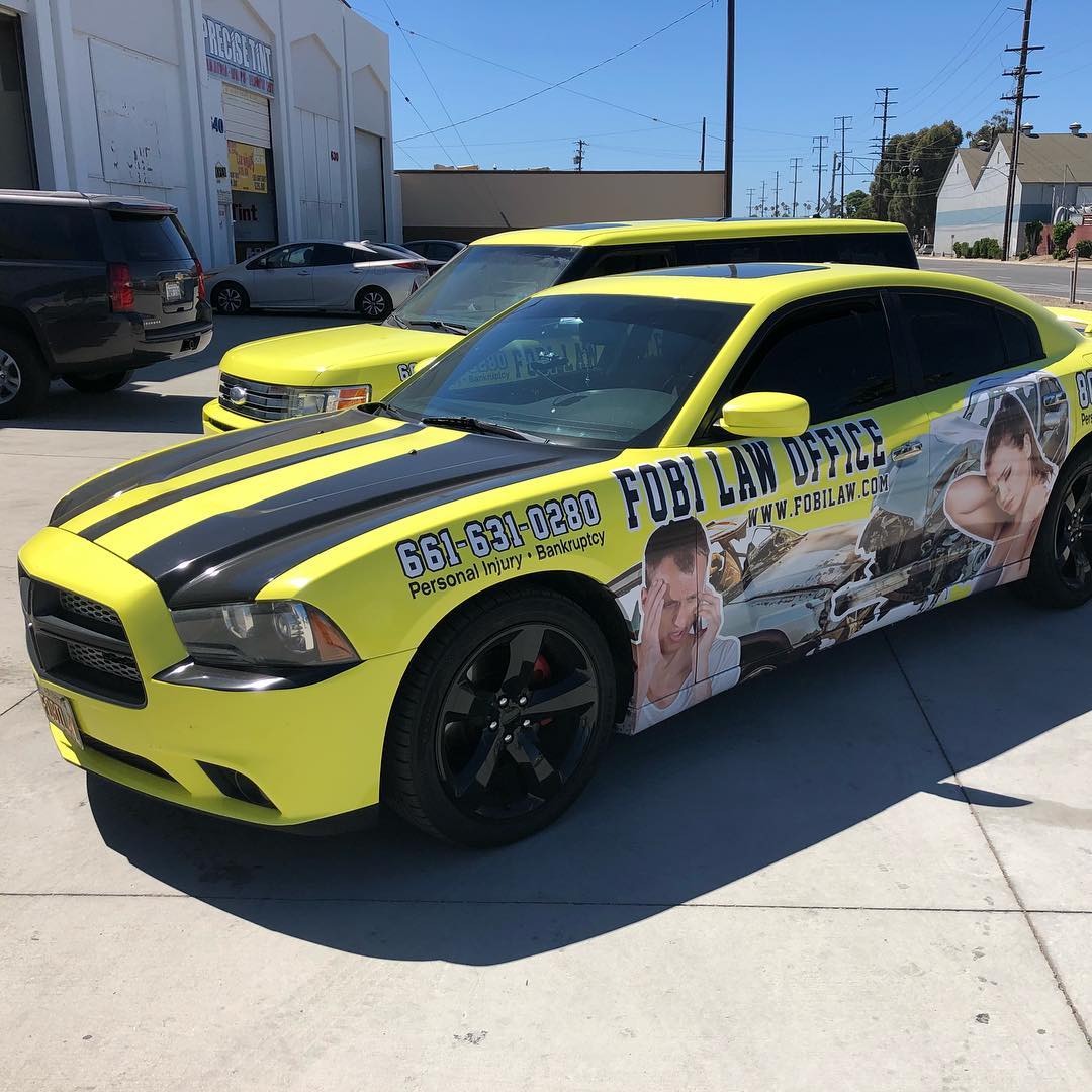 A yellow car with a black stripe on the hood is parked on the side of the road.