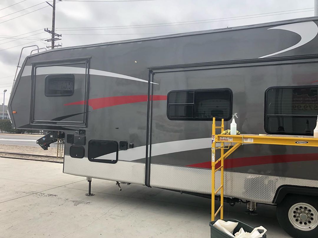 A large rv is parked in a parking lot next to a yellow ladder.