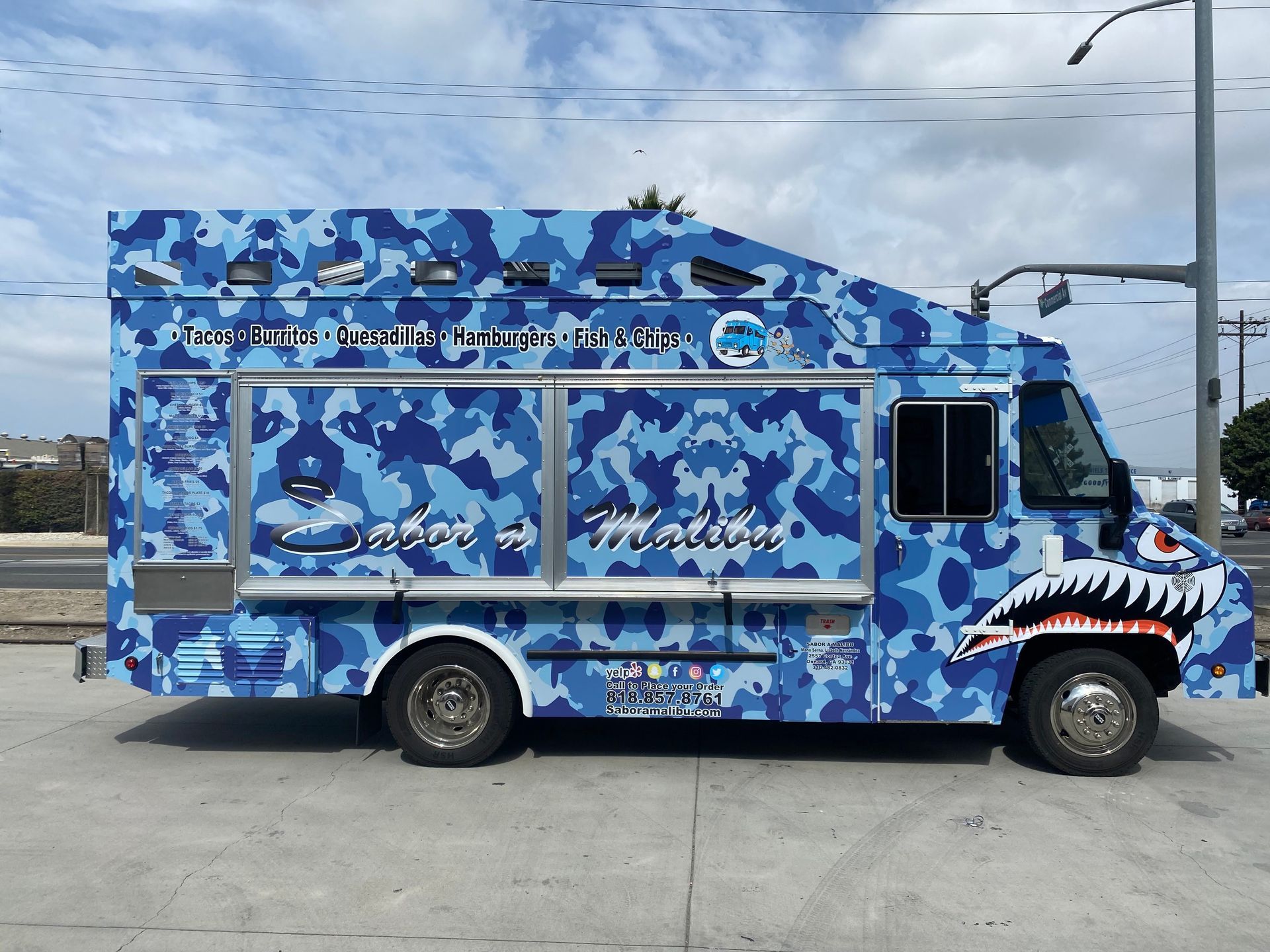 A blue camo food truck is parked on the side of the road.