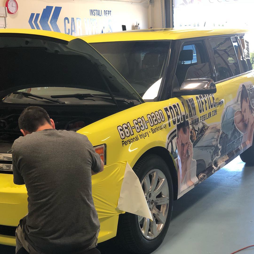 A man is working on a yellow car with a wrap on it