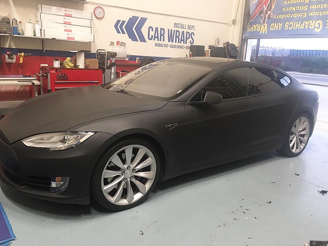 A black tesla model s is sitting in a garage.