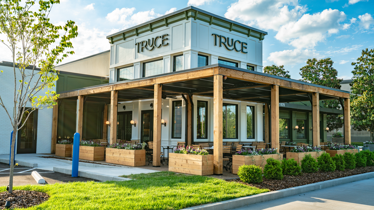 Modern TruC building with glass storefront, wooden porch, and landscaped lawn on a sunny day