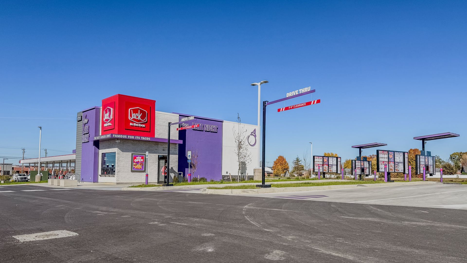 A Taco Bell restaurant with a purple and red facade and drive-thru lanes under a clear blue sky.