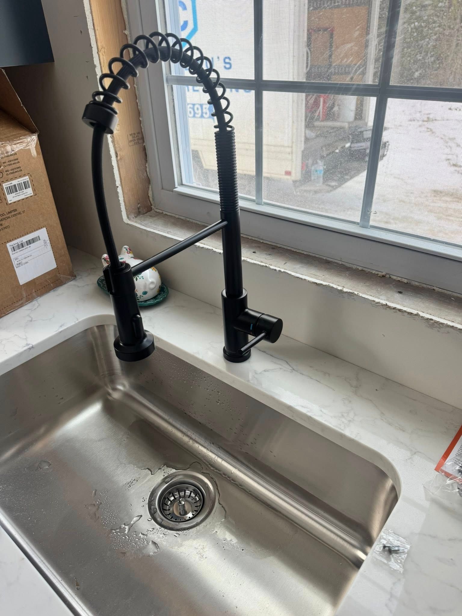 Stainless steel kitchen sink with a tall black spring-coil faucet by a window, with water droplets in the basin.