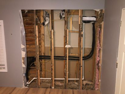 Wall opening revealing studs, pipes, electrical wires, and insulation.