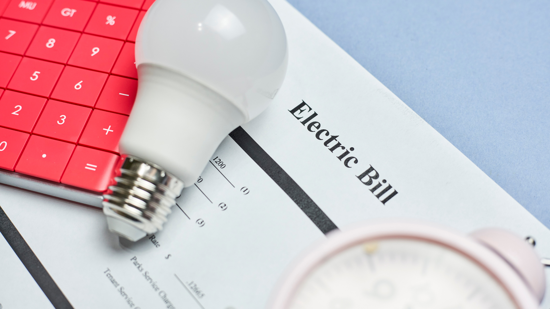 Red calculator and lightbulb on an electric bill next to a clock.