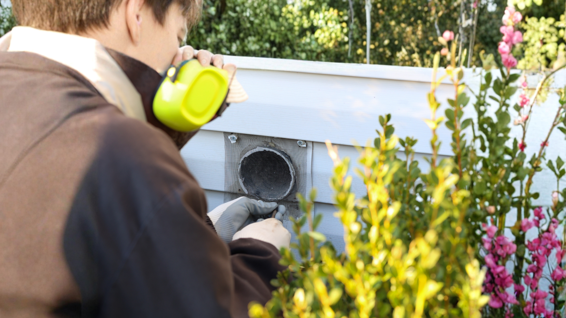 Person cleaning a vent on a house exterior; uses a handheld tool.
