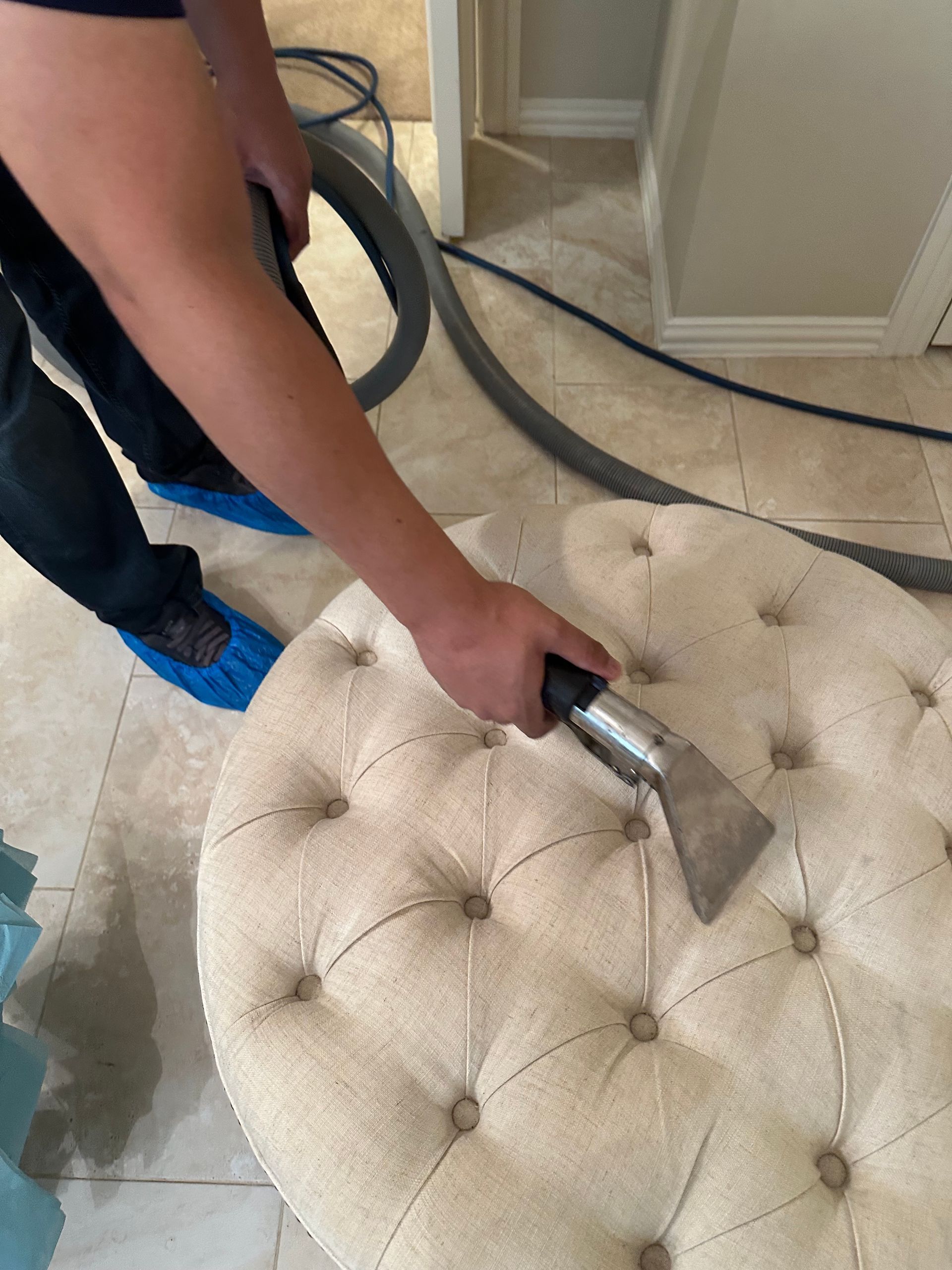 Vacuuming green upholstered chair with a handheld nozzle; gray couch in background.