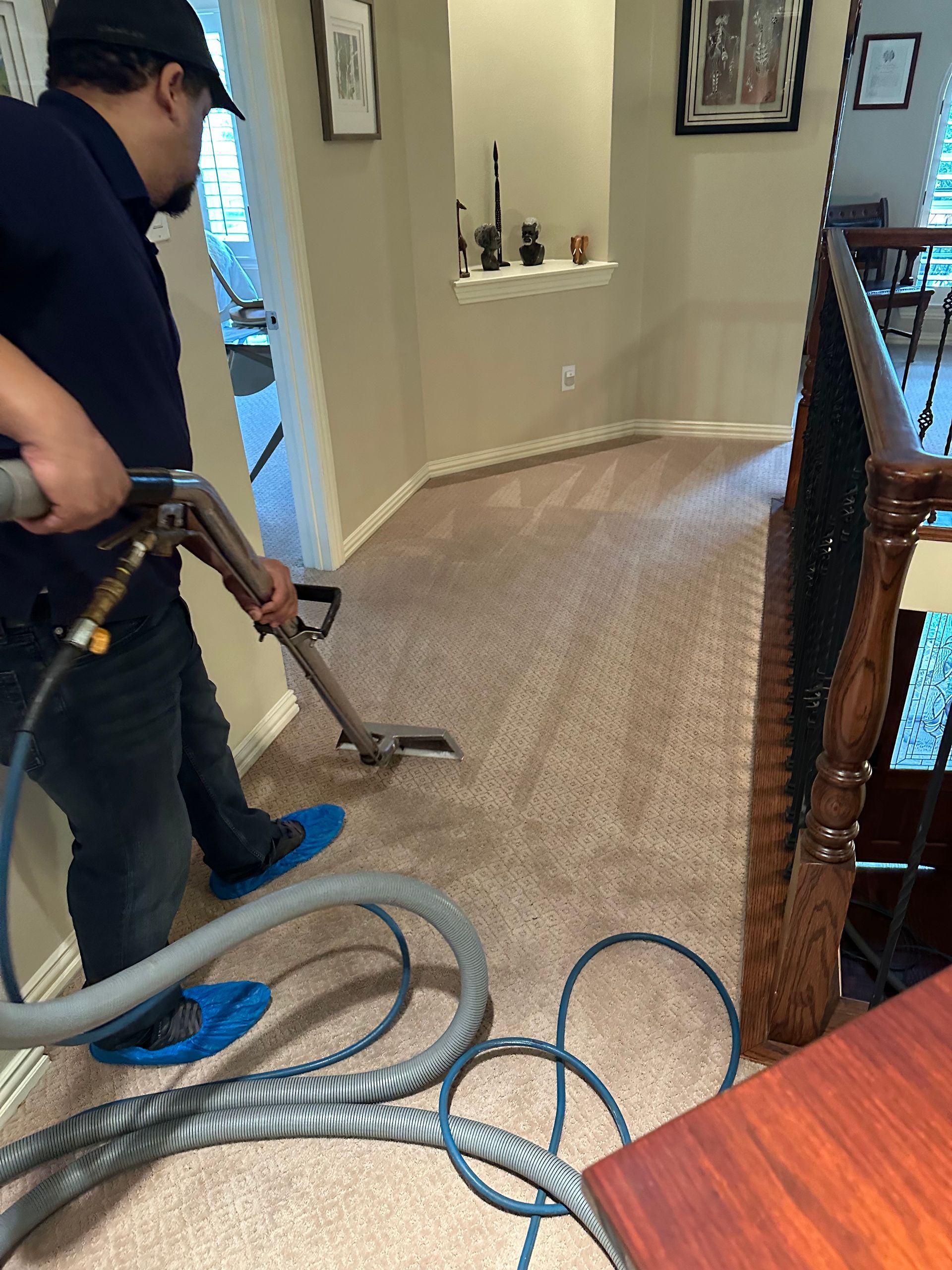 Vacuum cleaner cleaning a patterned carpet; person's legs and white shoes visible in the background.