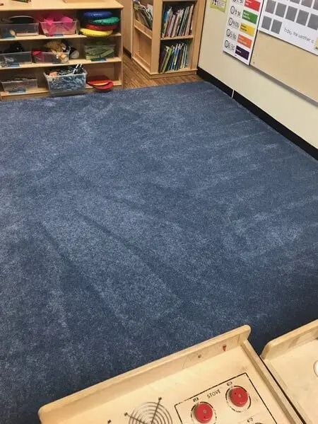 Blue carpet in a classroom setting, partially showing shelves with books and toys.
