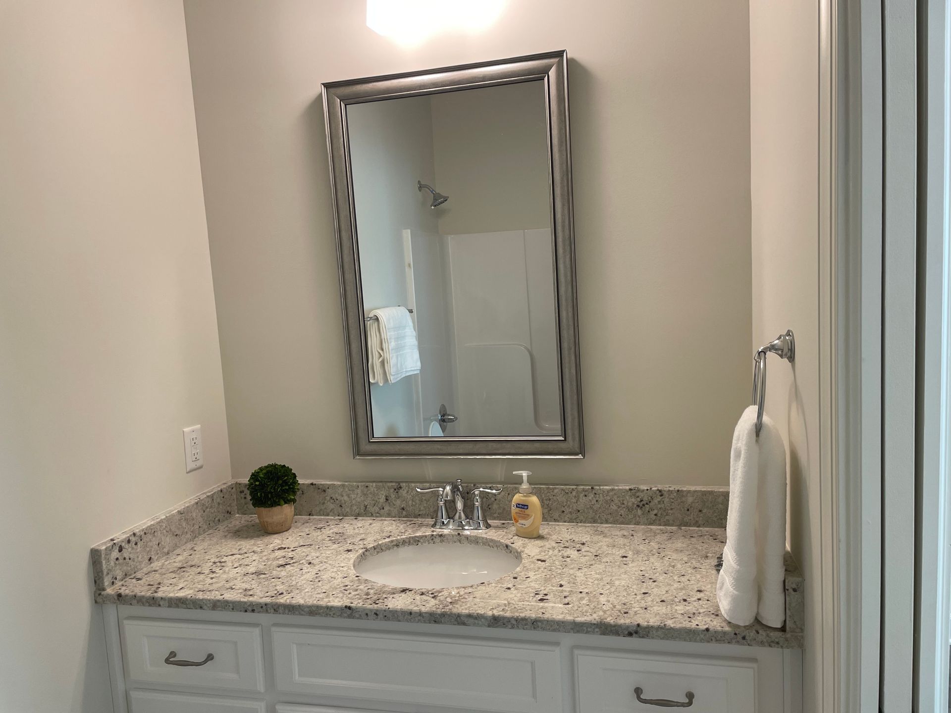 Bathroom with white vanity, speckled countertop, large mirror, and towel rack.