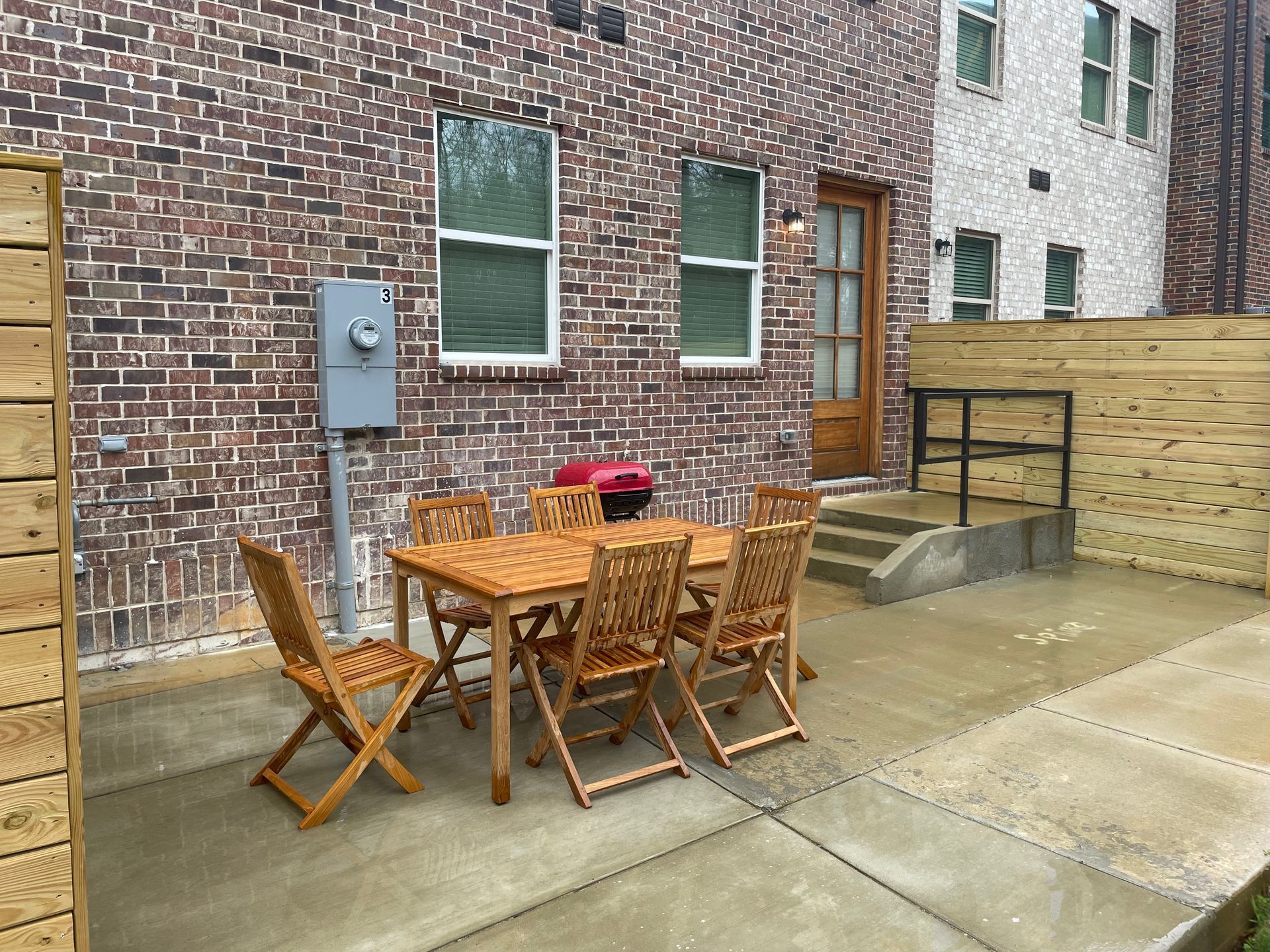 Patio with wooden furniture, brick wall, and small grill.