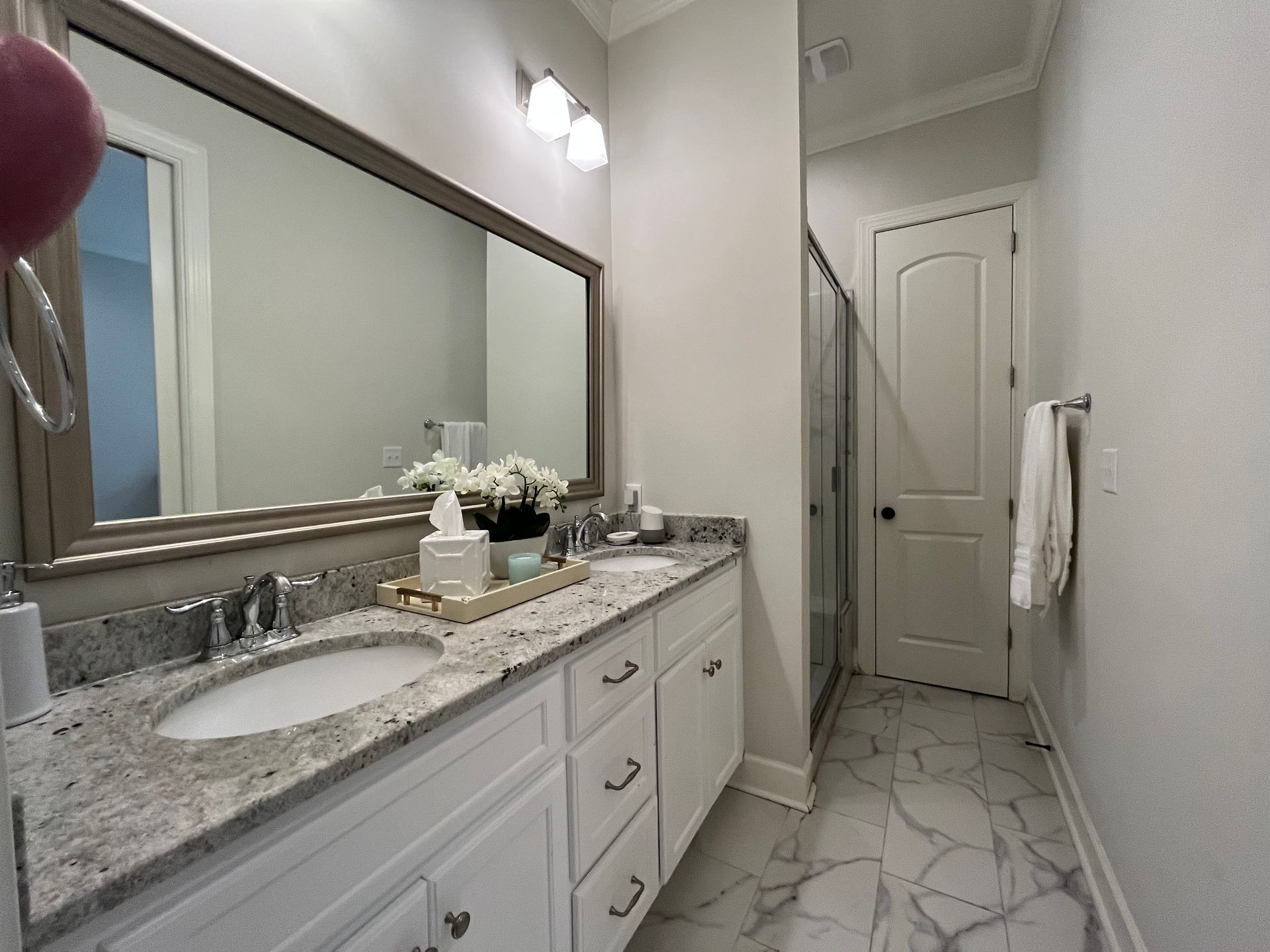 Bathroom with a white vanity, marble countertop, large mirror, and glass shower door.