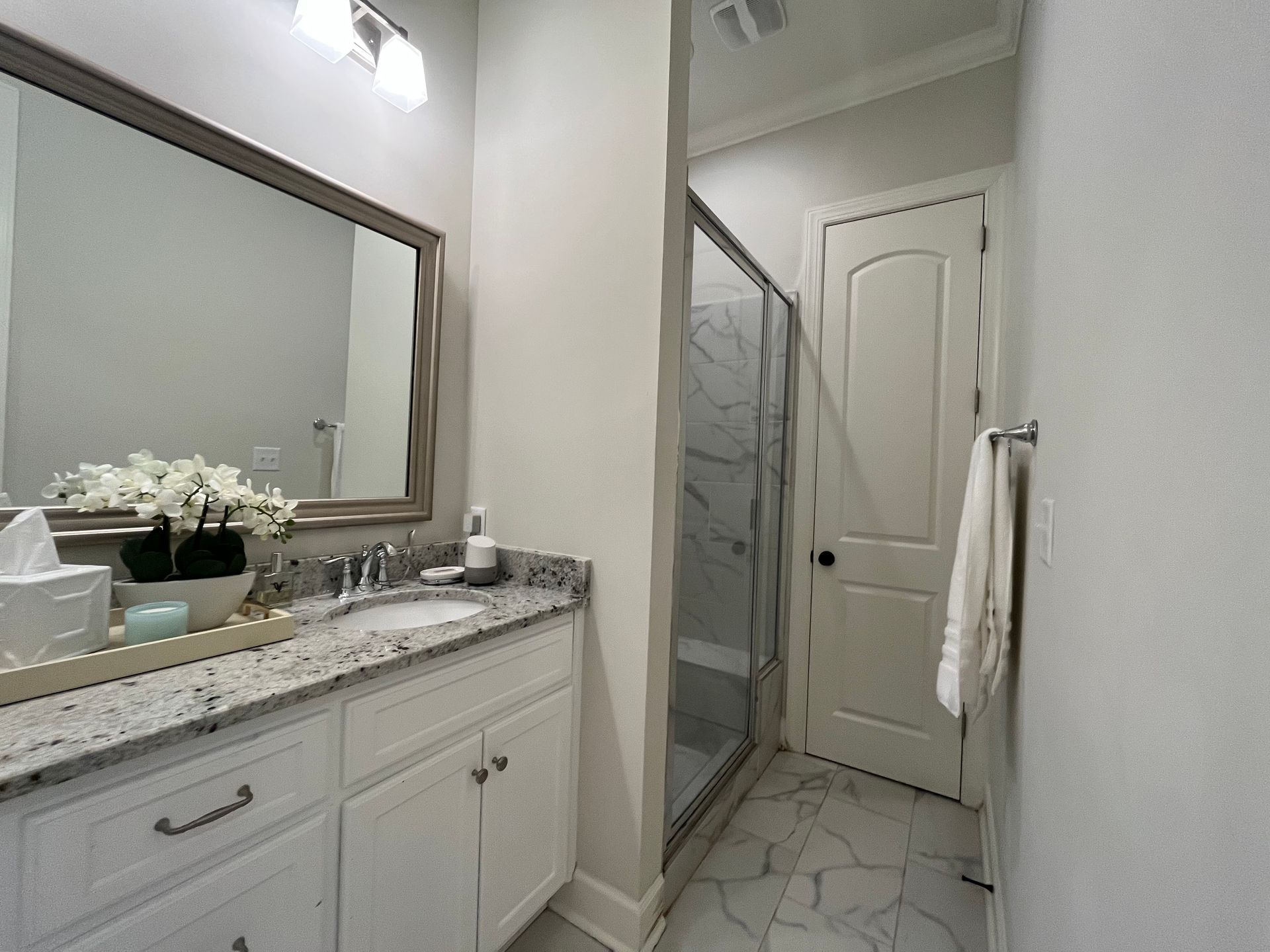 Bathroom with white cabinets, marble countertop, large mirror, and glass shower.