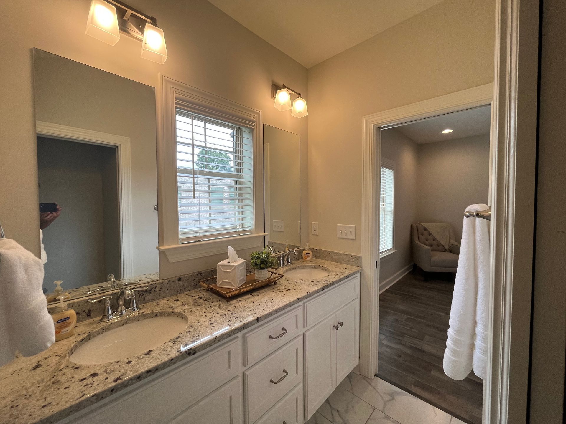 Bathroom with double vanity, two mirrors, and an open doorway to a sitting area.