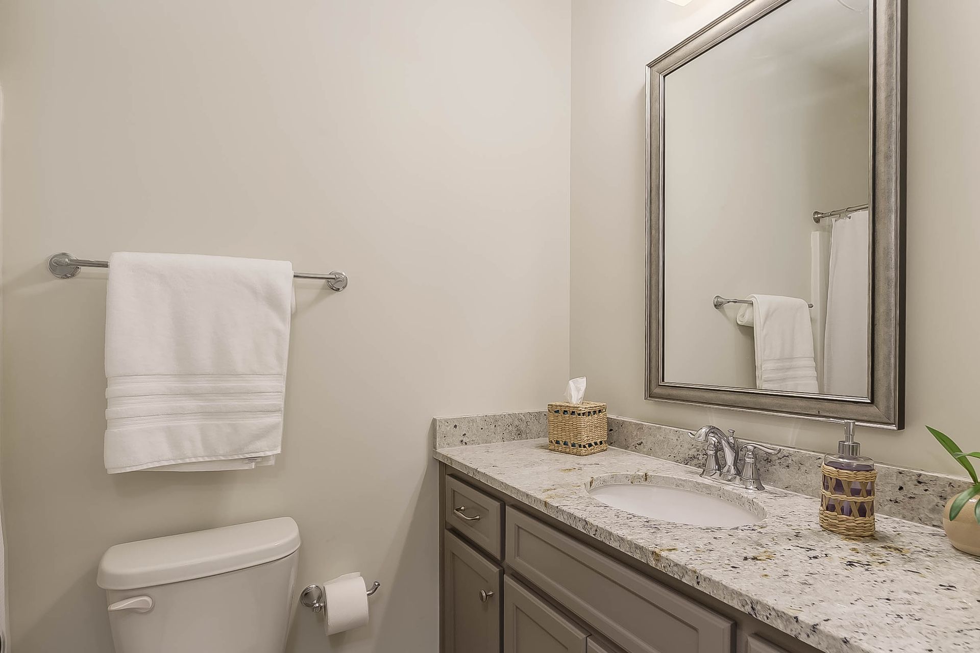 Bathroom with toilet, sink, mirror, towel rack, and light-colored walls.