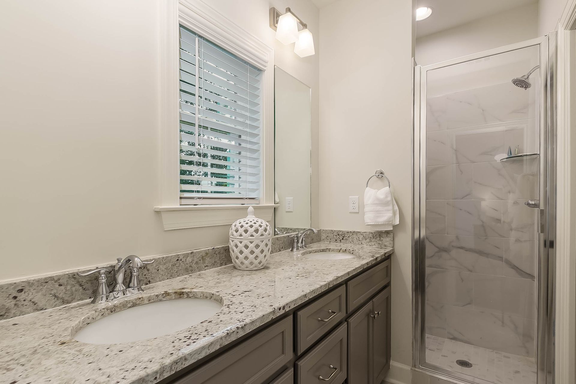 Bathroom with double sink vanity, gray cabinets, marble countertops, and a glass shower.