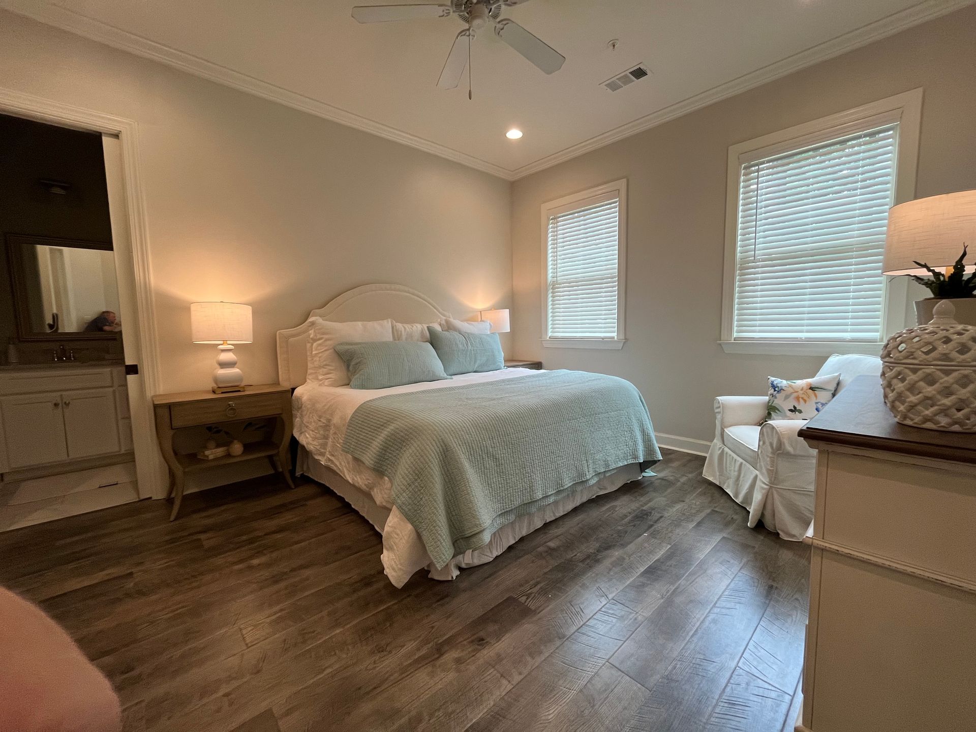 Bedroom with queen bed, white nightstands, wood floor, and armchair.