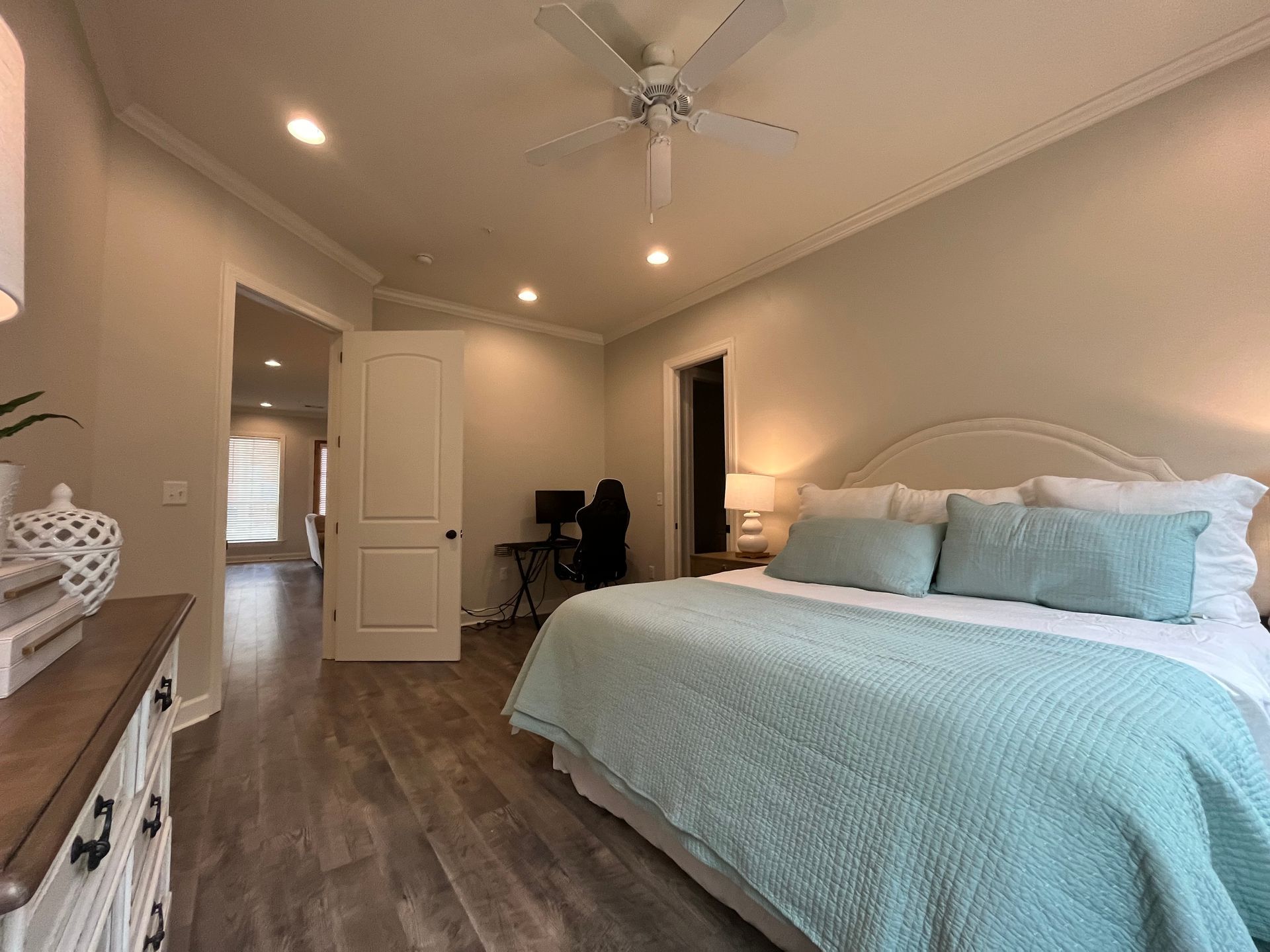 Bedroom with a bed, dresser, and desk. Pale walls, wood floors, and a ceiling fan.