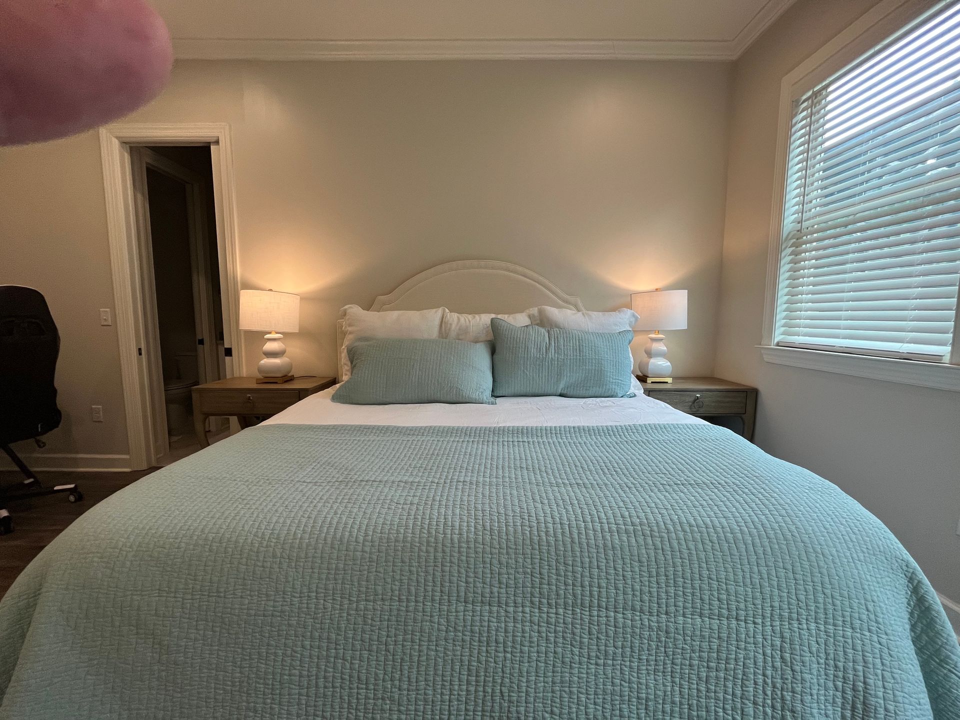 Bedroom with light-blue bedspread, two nightstands, two lamps, and a window with blinds.